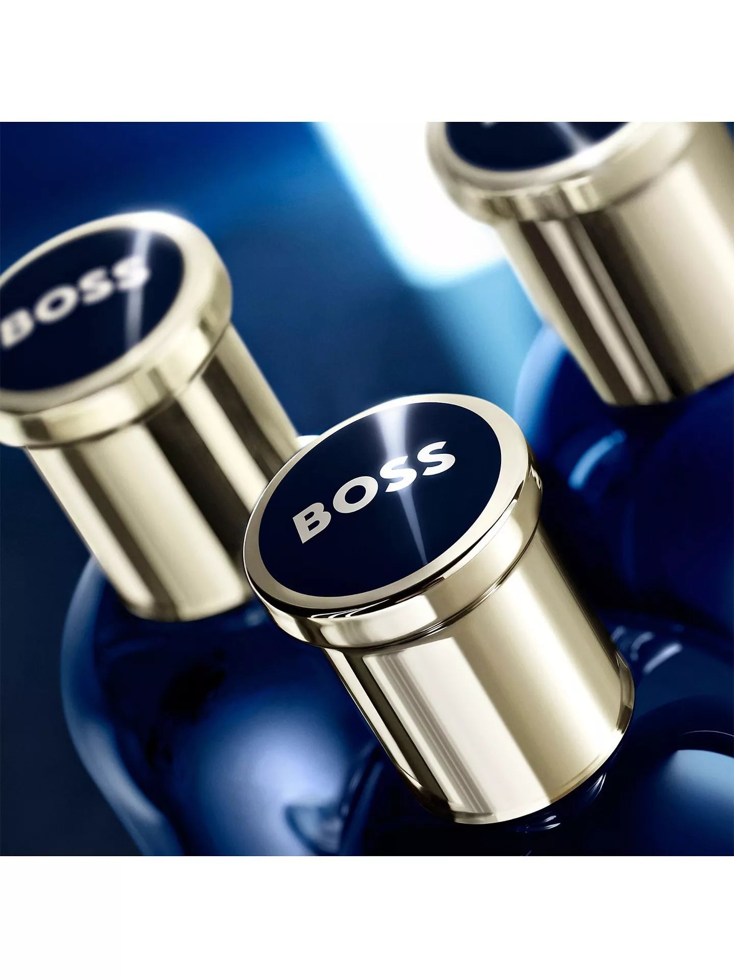 Two blue bottles with gold caps featuring the 'BOSS' logo on a dark background.